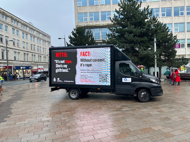 A Transit Media digital advertising van parked in Liverpool city centre displaying a Merseyside Police campaign panel reading 'MYTH: It's not rape, she's my girlfriend' alongside the fact 'Without consent, it's rape'