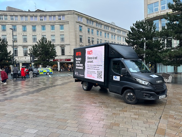 A Transit Media digital advertising van in Liverpool's Derby Square displaying a Merseyside Police campaign panel with the myth 'She didn't say no, it must mean she wanted it' and the fact 'Silence is not consent'